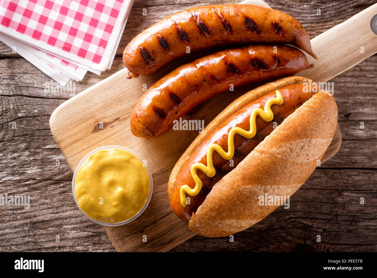 Delicious grilled smoked sausages on a roll with yellow mustard. Stock Photo