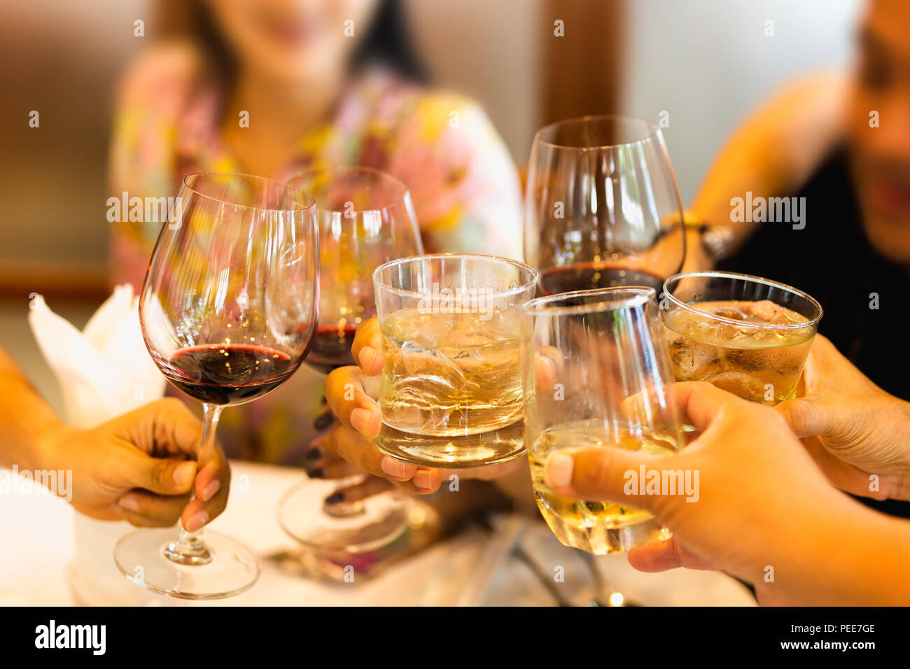 Group of friends raising a toast with glasses of red wine and whiskey at family dinner Stock Photo