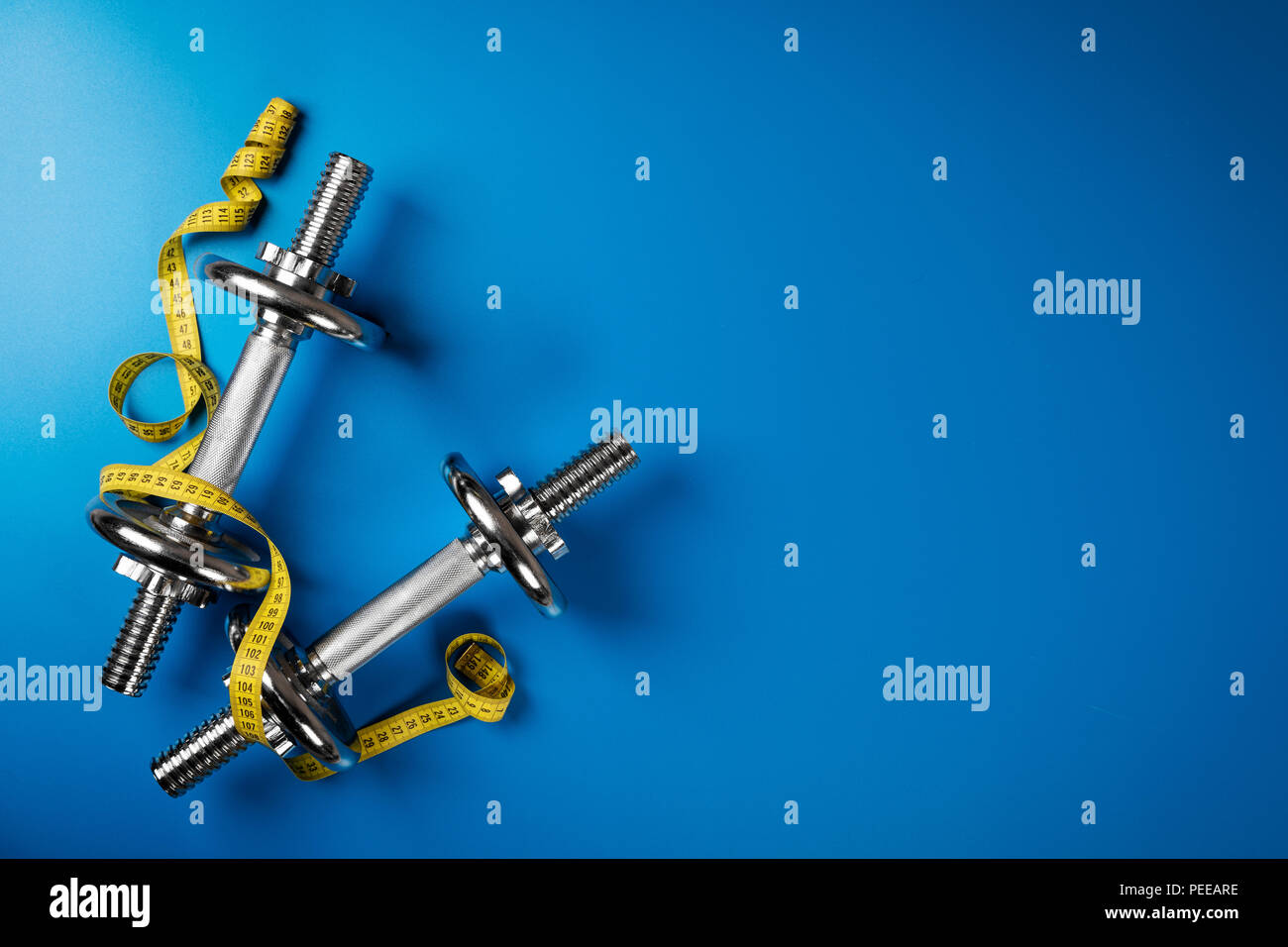 dumbbells and measuring tape on blue background with copy space Stock Photo