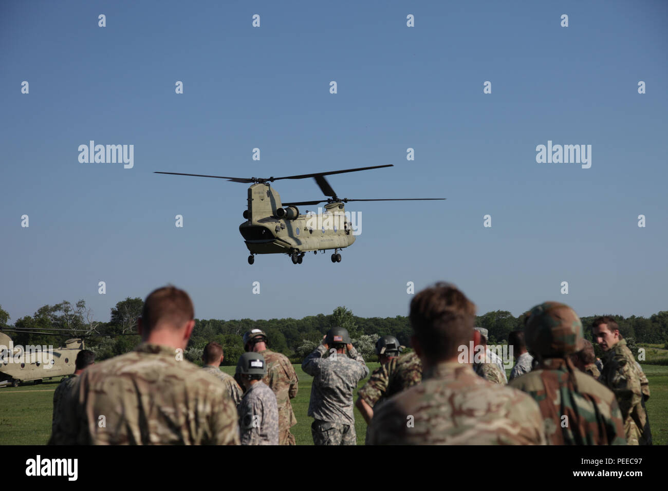 Paratroopers watch a CH-47 Chinook land prior to a wing exchange jump at Leapfest in West Kingston, R.I., Aug. 3, 2015. Leapfest is an International parachute competition hosted by the 56th Troop Command, Rhode Island National Guard to promote high level technical training and esprit de corps within the International Airborne community. (U.S. Army Photo by Spc. Josephine Carlson/Released) Stock Photo