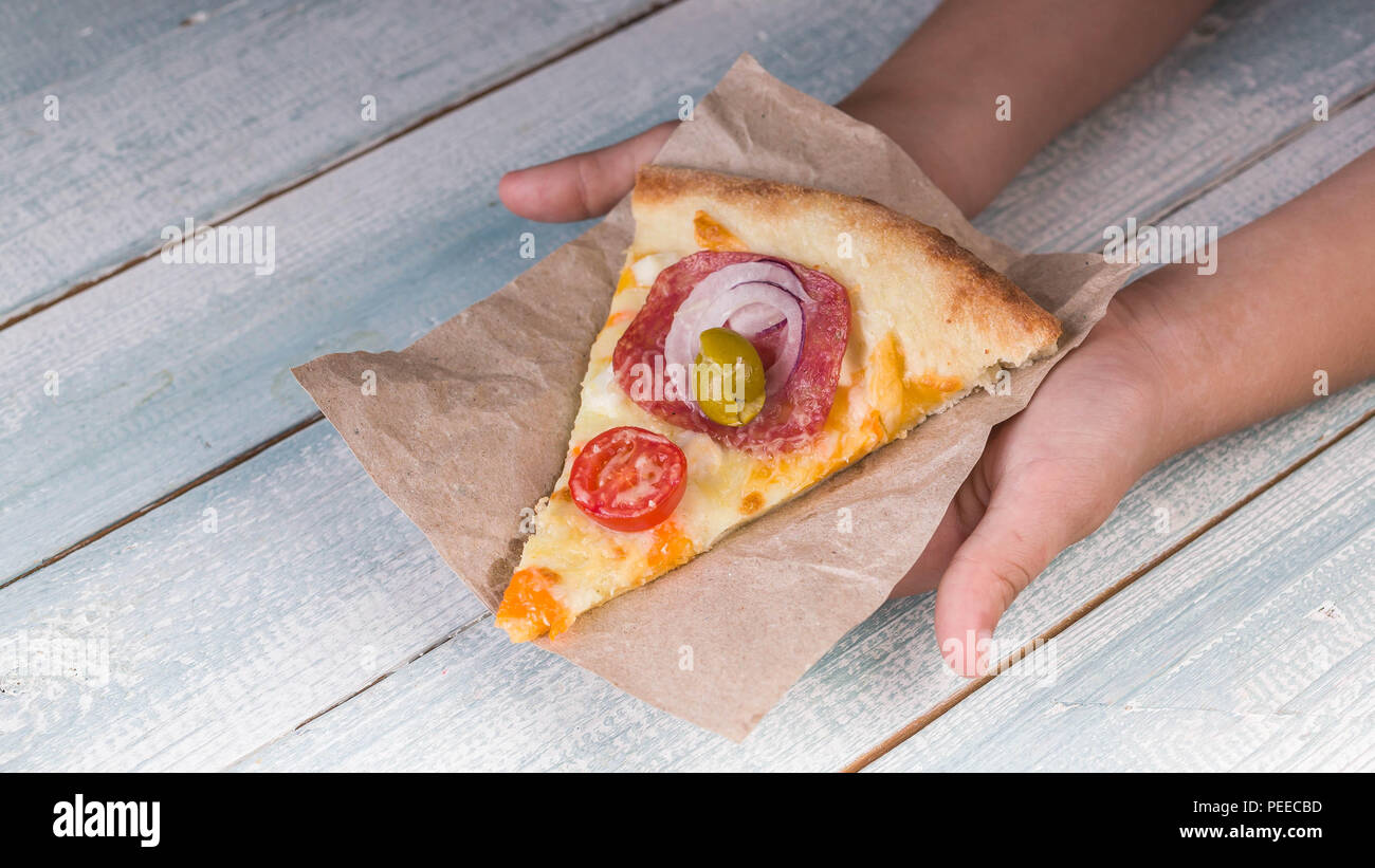 Children's hands hold a slice of pizza. Wooden background Stock Photo