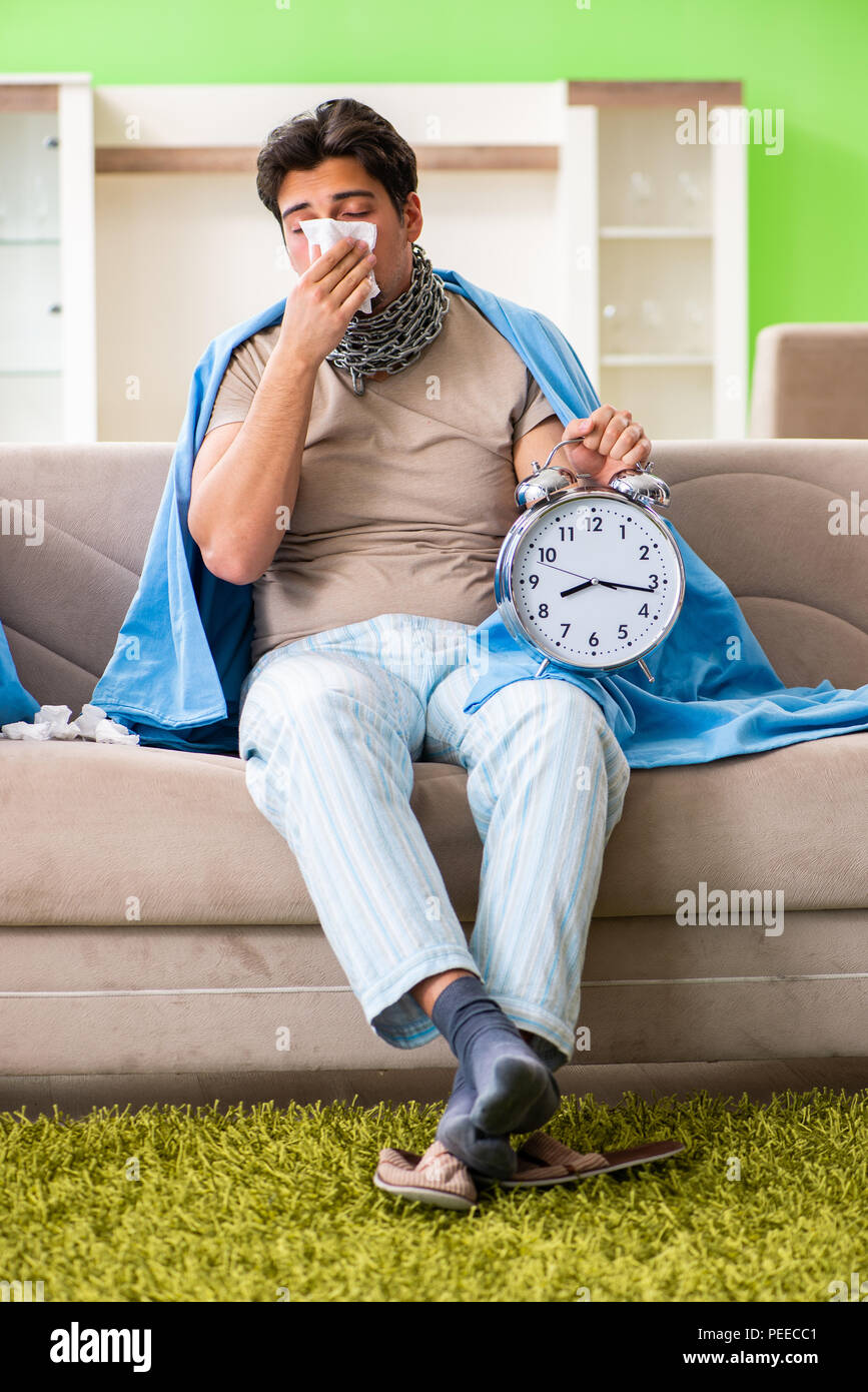 Sick young man suffering from flu at home in time management concept Stock Photo