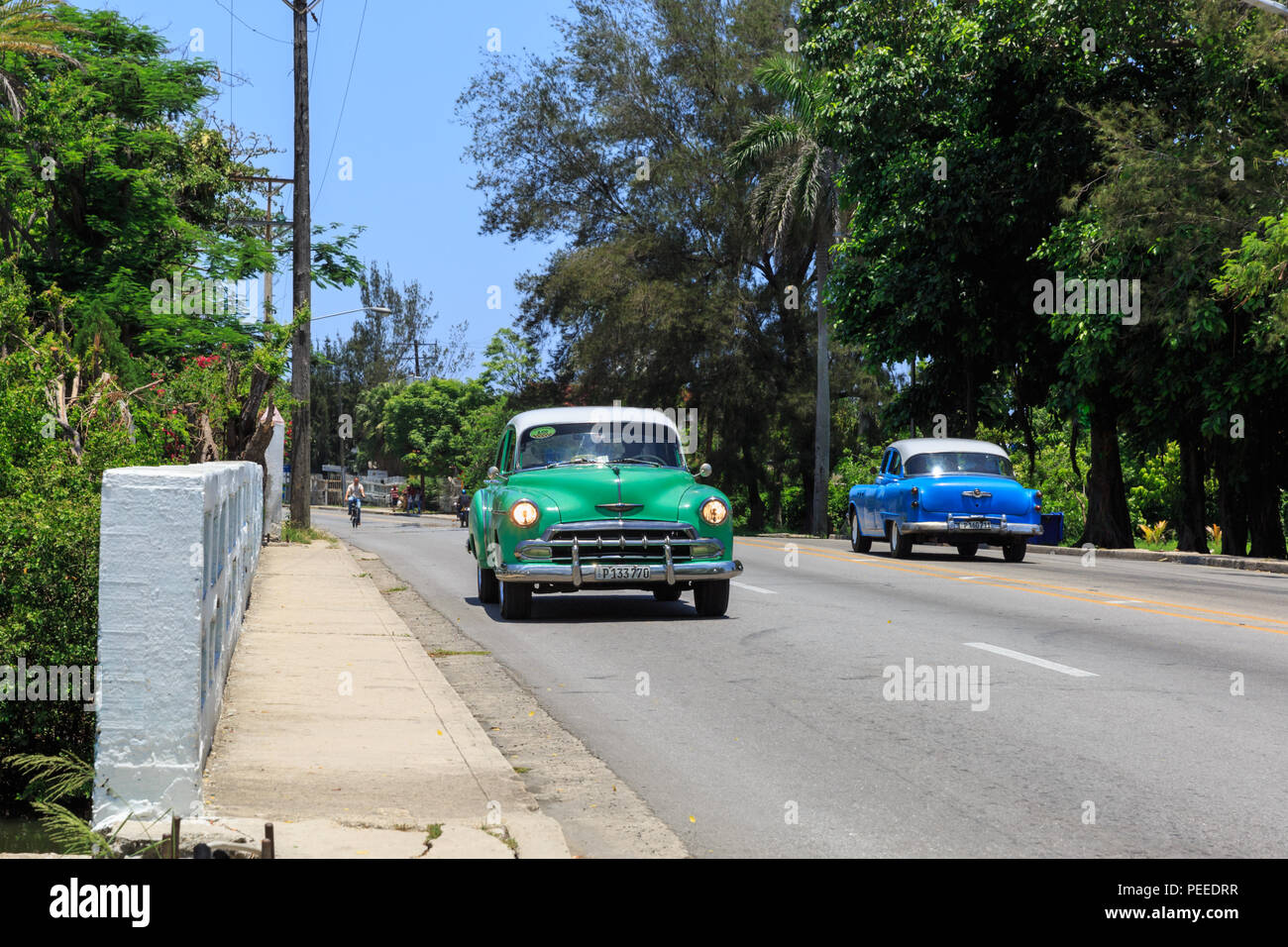 Rural scene, American classic cars and vintage automobiles travelling on a road in Cuba Stock Photo