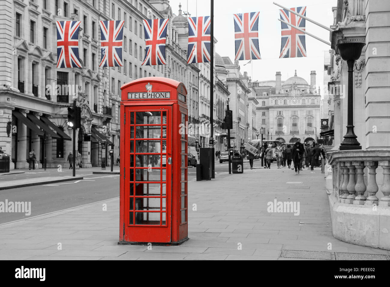 A traditional British red telephone box is standing on the street. Six British flags are hanging above it.  Booth and flags isolated in a black and wh Stock Photo