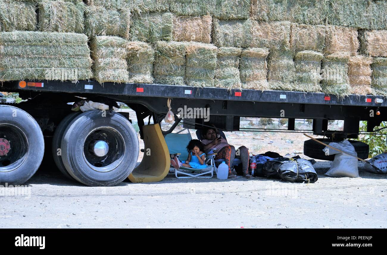Mother and daughter sitting under a semi truck bed carrying bales of hay on the side of the road in Tecate, Baja California, Mexico. Stock Photo