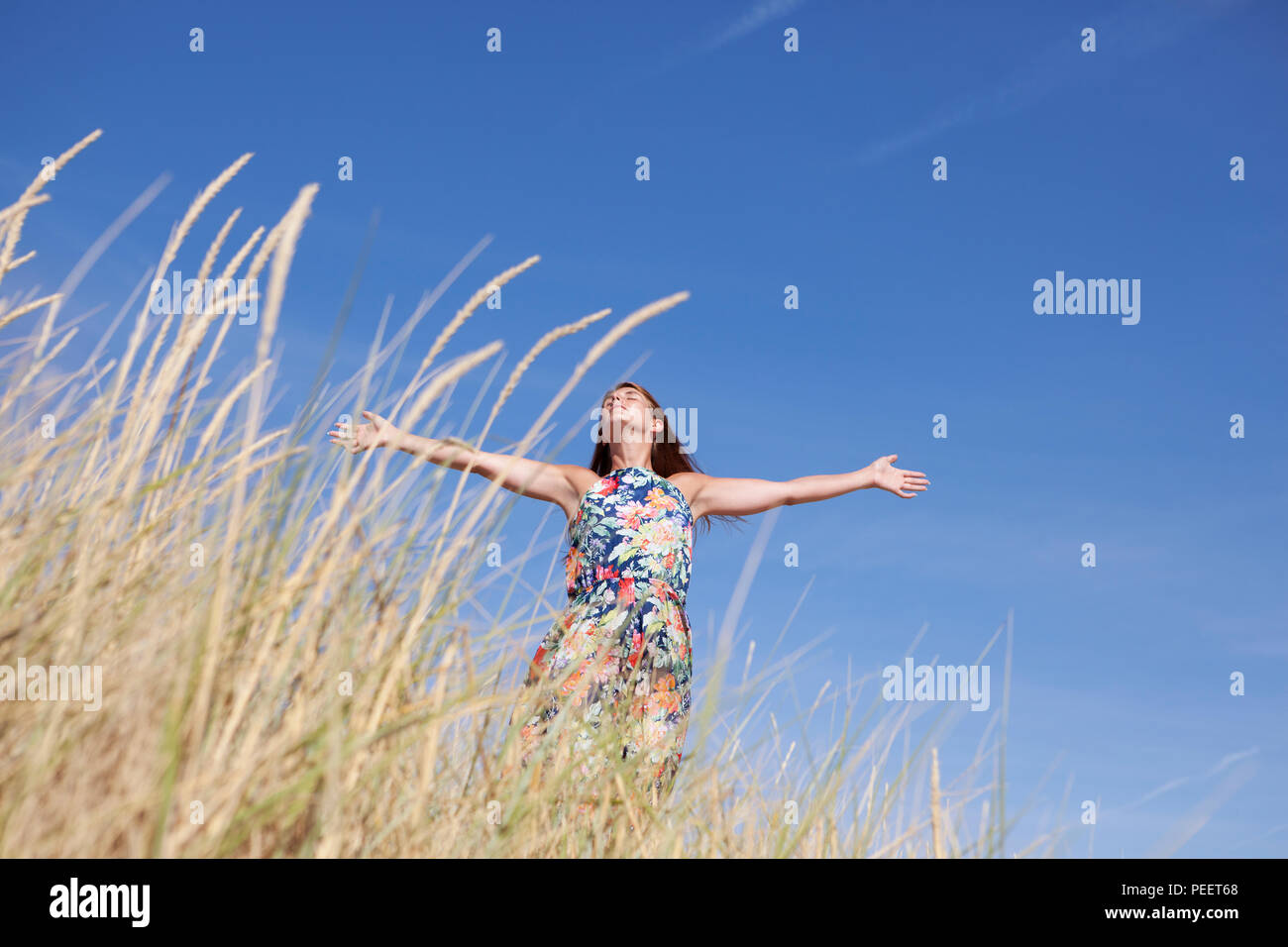 a young woman with long hair and a colorful dress enjoys the summer on the beach Stock Photo