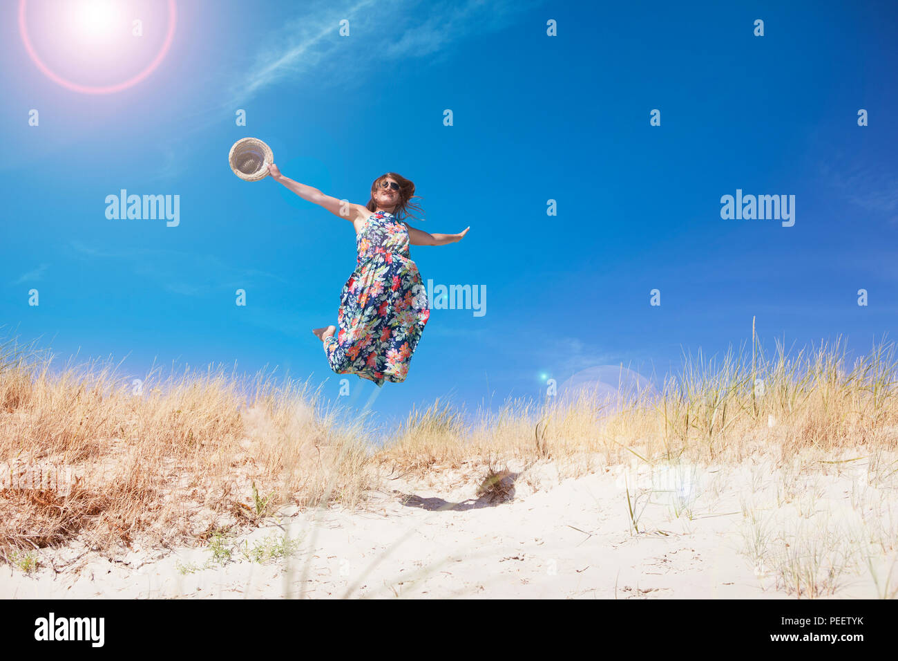 a young woman with long brown hair and sunglasses on the beach. jumps in the air Stock Photo