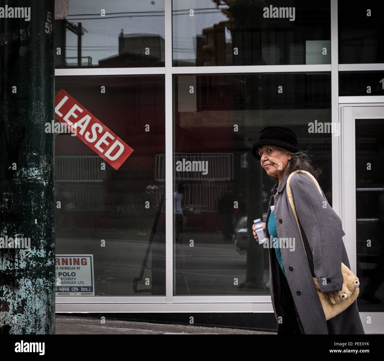 VANCOUVER, BC, CANADA - MAY 11, 2016: A woman walks past a newly leased retail space in Vancouver's Downtown Eastside an area which is plagued with homelessness, drug use, and poverty. Stock Photo