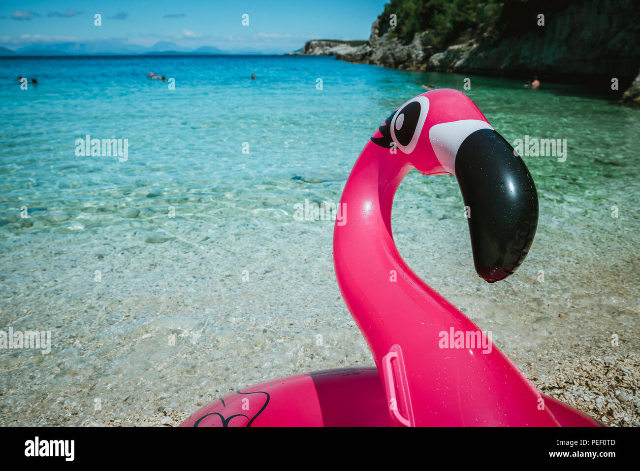 Air flamingos balloon float in Dafnoudi beach in Kefalonia, Greece. Remote lagoon with pure clean turquoise sea water, white rocks and cypress trees Stock Photo