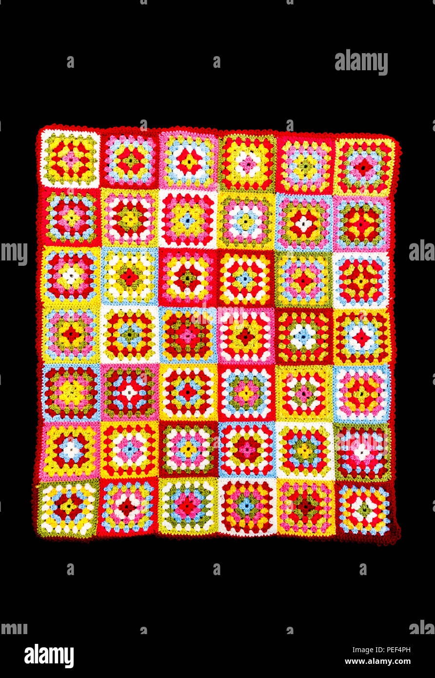 Brightly coloured rectangular granny square woollen baby blanket, traditional hand made crochet home handicraft, against a black background Stock Photo