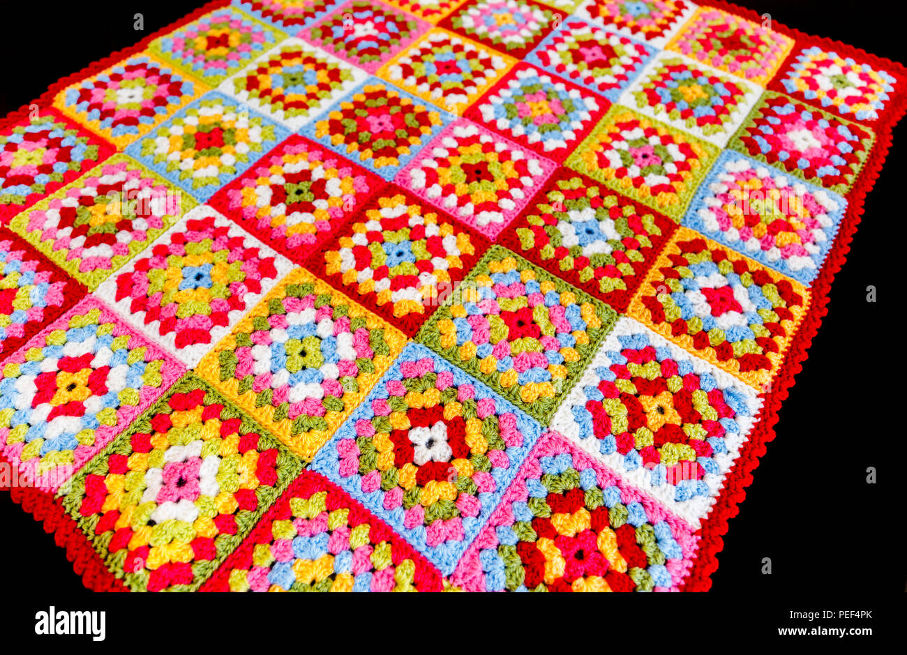 Brightly coloured granny square woollen baby blanket, traditional hand made crochet home handicraft, against a black background Stock Photo