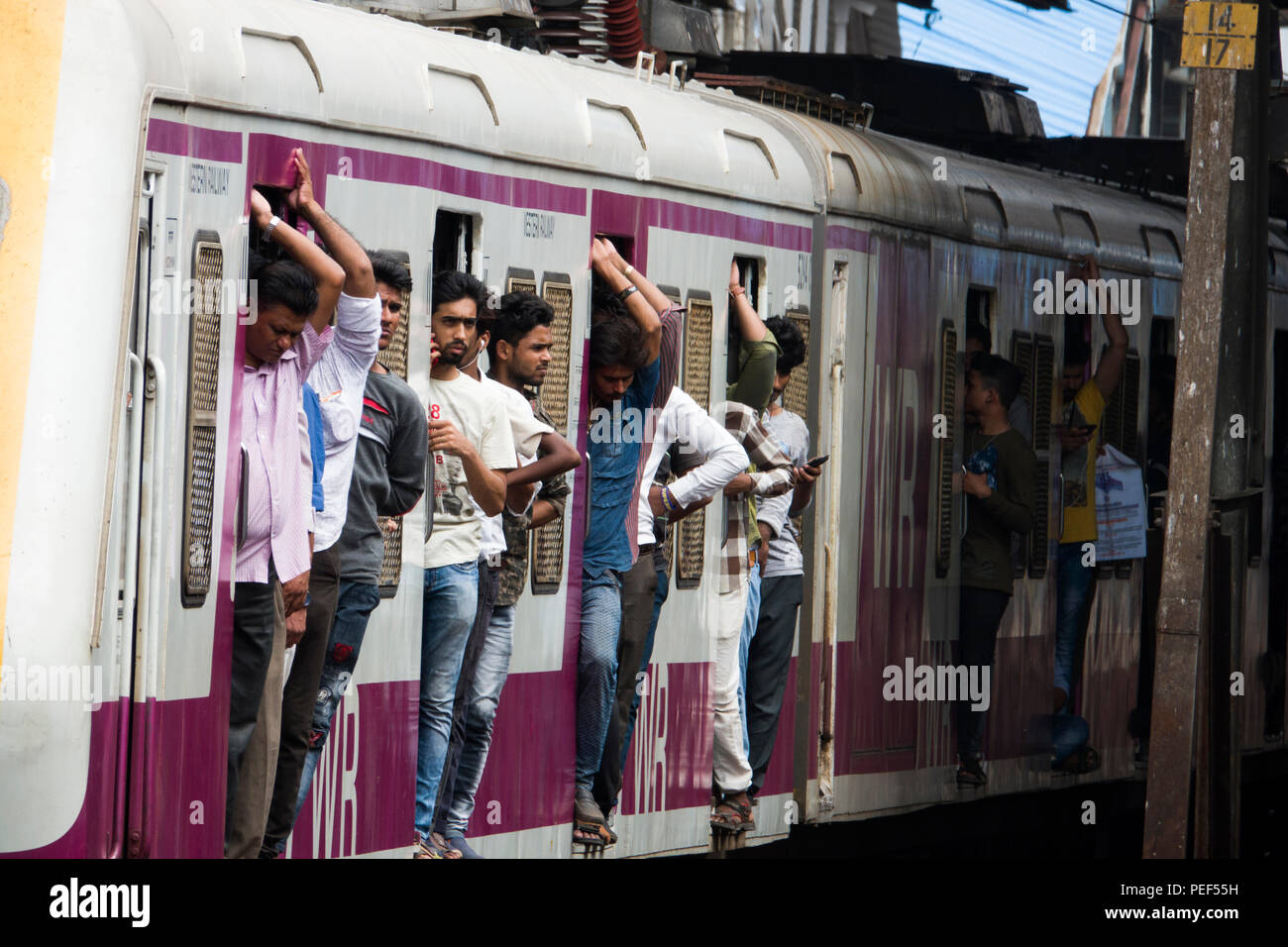 Passengers hanging out of trains door on a Mumbai Suburban Railway train at Bandra station in Mumbai, India Stock Photo