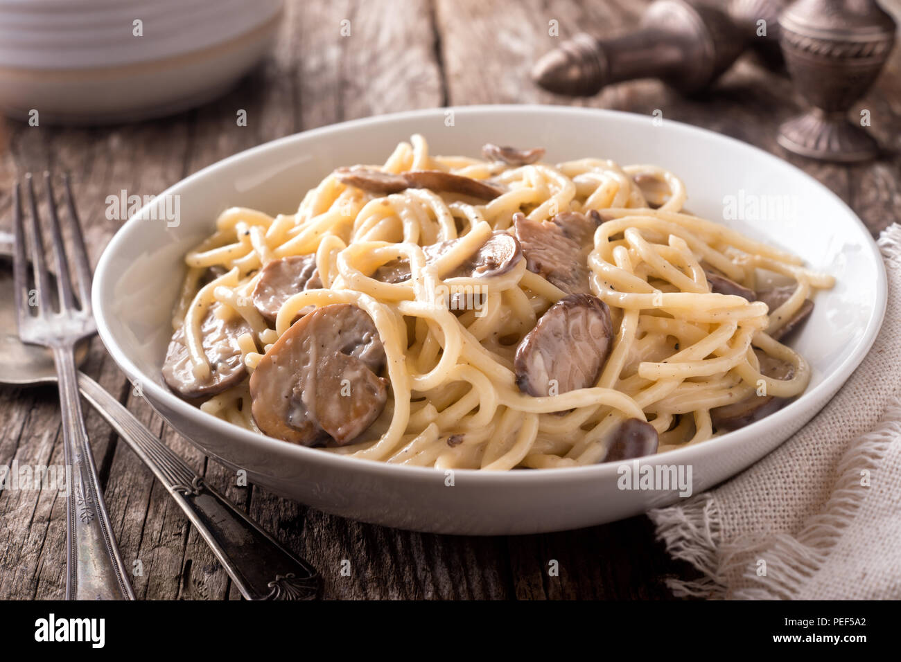 A bowl of delicious pasta alfredo with mushrooms on a rustic table top. Stock Photo