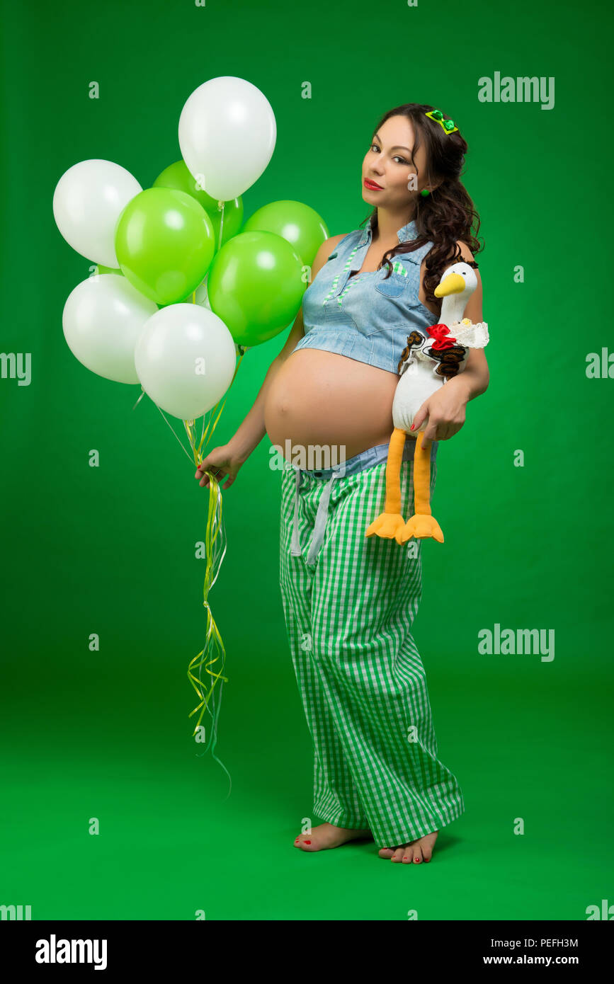 Pregnant Woman With Balloons And Stork On A Green Background He Looks At His Tummy In