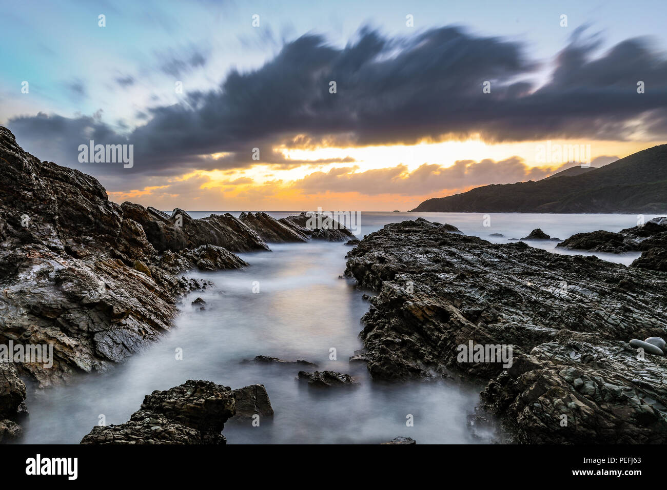 Cloudy sunrise over ocean and rocky beach Stock Photo - Alamy