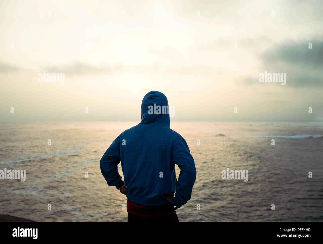 Man wearing a hoodie from behind thinking of his epic journey around the world. Golden sunset in Punta Hermosa beach town.Lima Province,Peru. Jul 2018 Stock Photo