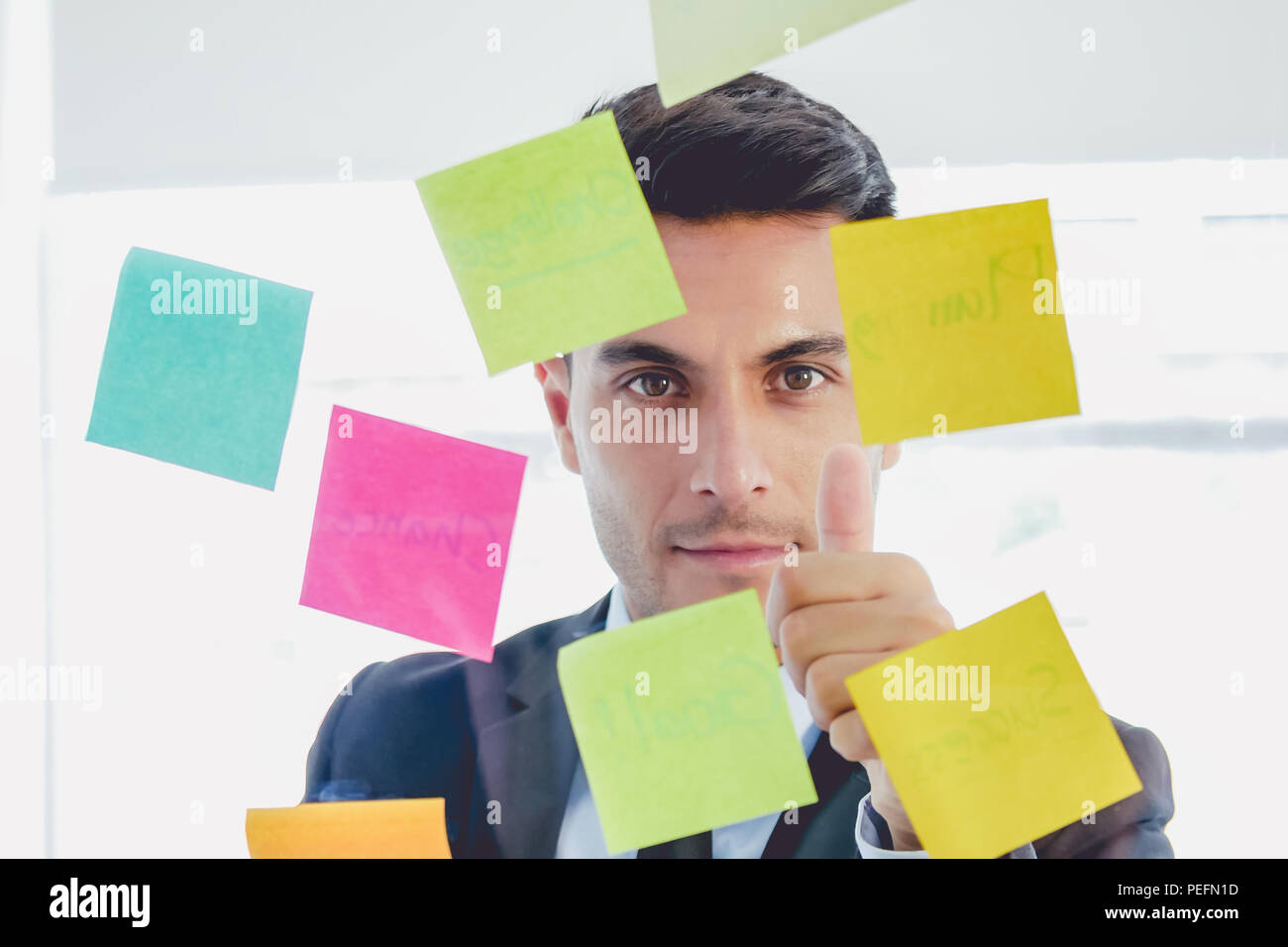 Handsome startup businessman looking straight sticky notes and thumb up in glasses stands in creative office Stock Photo