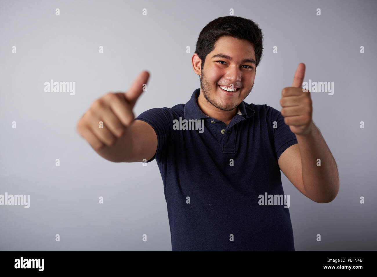 Smiling hispanic man with thumbs up isolated on gray background Stock Photo