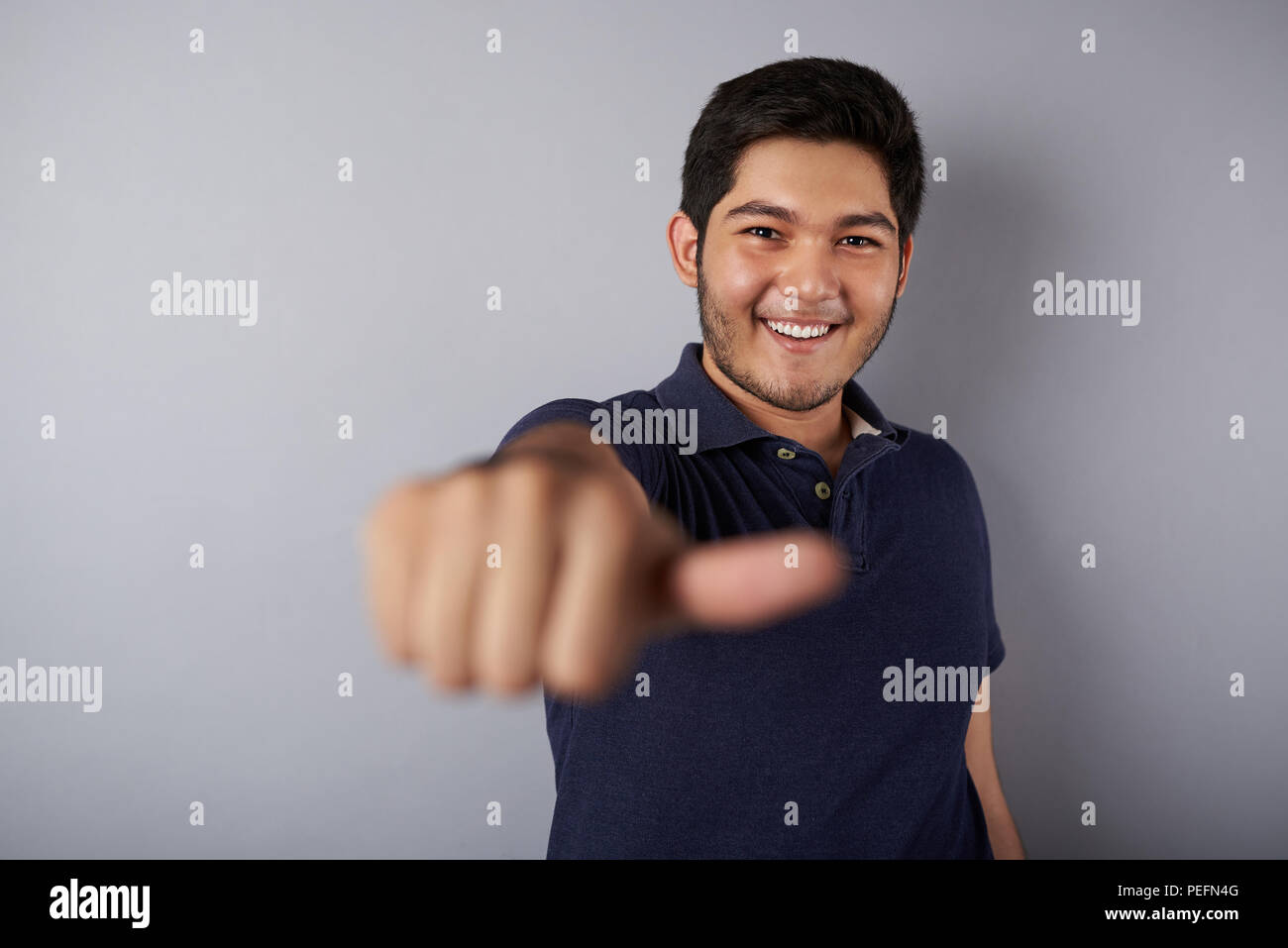 Smiling man showing thumb up into camera on gray background Stock Photo