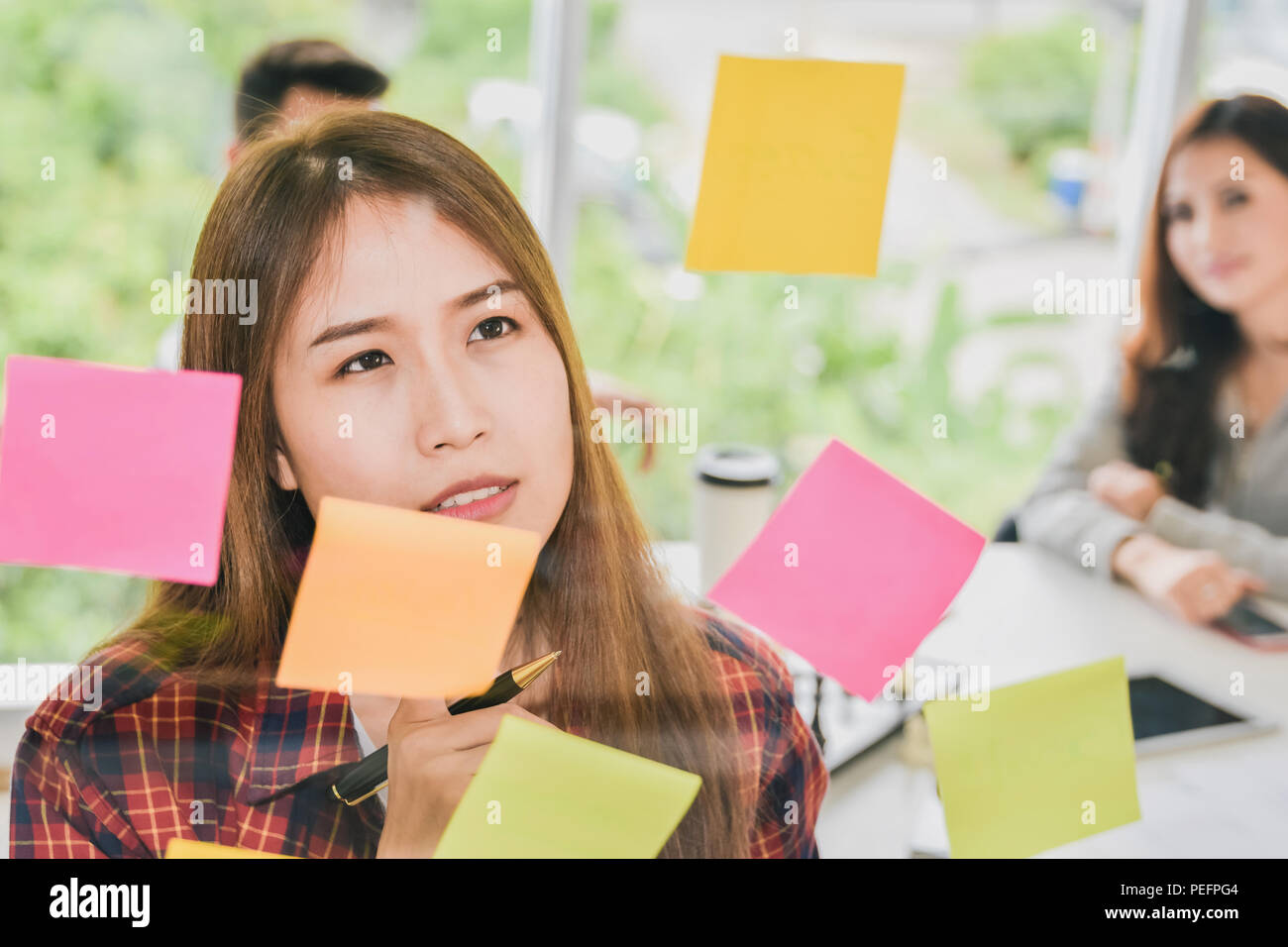 Thoughtful businesswoman looking at sticky notes stuck and thinking on glass wall in creative office Stock Photo
