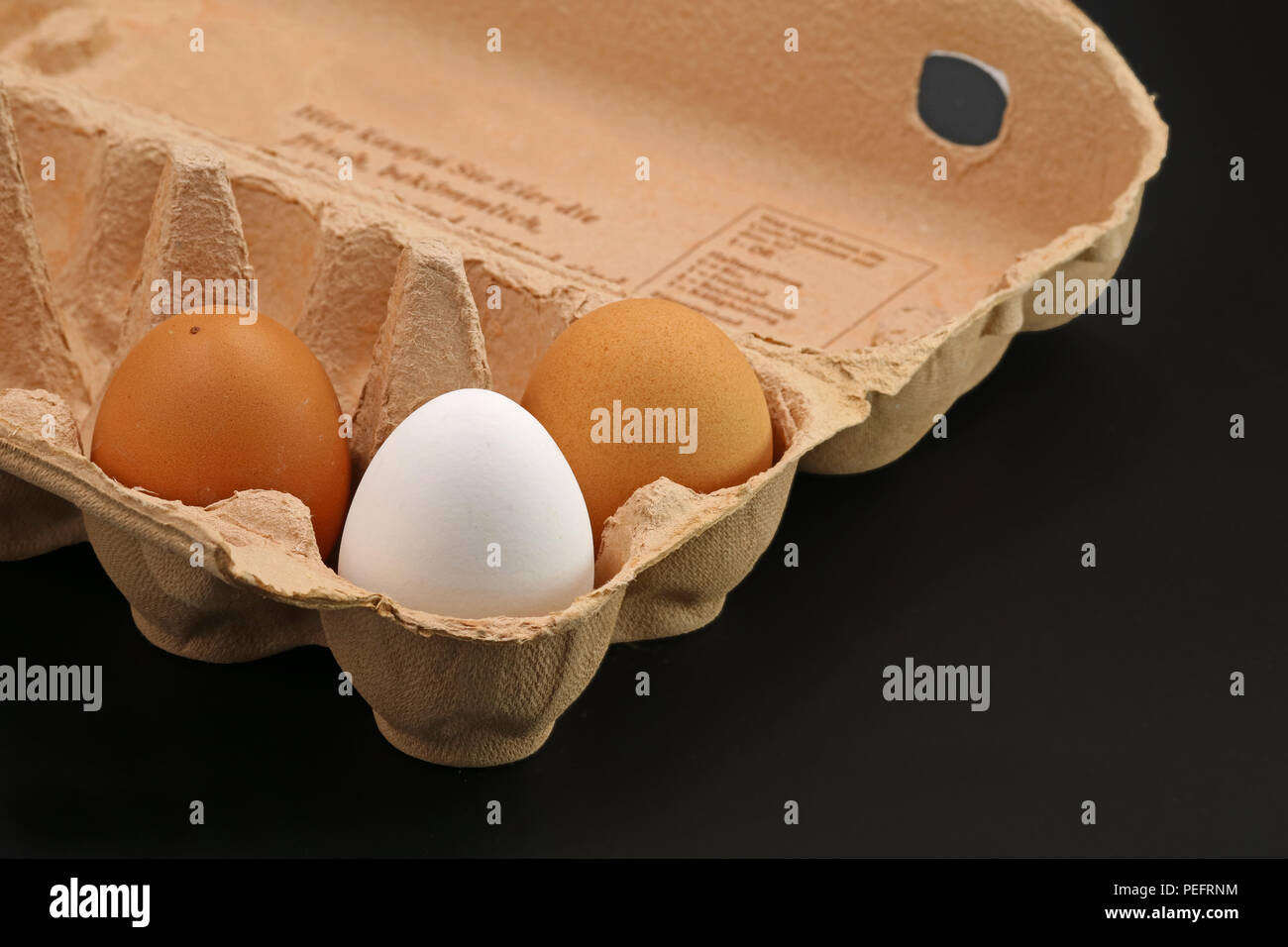 Three Brown Eggs In A Grey Cardboard Box on black background Stock Photo