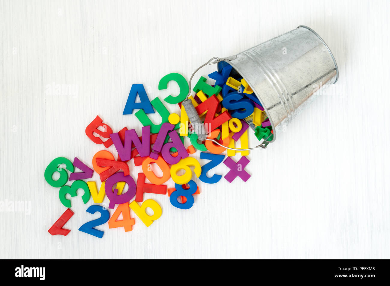 Colorful plastic numbers and letters falling from metal bucket Stock