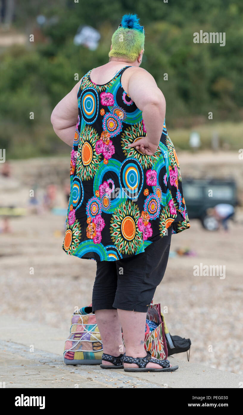 large obese woman dressed in colourful clothing with dyed hair with hands on hips at the seaside. Stock Photo