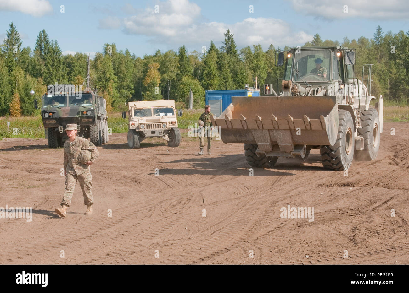 Pfc. Paola Mata, of Dallas, a heavy equipment operator with 500th Engineer Company, 15th Engineer Battalion, 18th Military Police Brigade based out of Grafenwoehr, Germany, ground guides Enlisted Jonas Sundberg, of Moss, Norway, an engineer with the Theater Enabling Force of the Norwegian Army High Readiness Force to a gravel mound near a road construction Aug. 19, at the Central Training Area near Tapa, Estonia. The efforts are a part of Operation Atlantic Resolve, an ongoing series of training operations and events designed to build relationships, trust and interoperability between the U.S.  Stock Photo