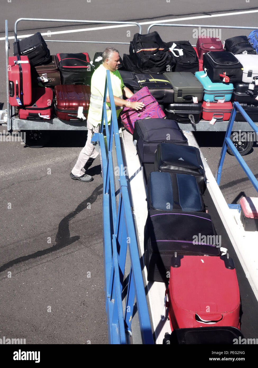 Airport handler loading baggage being put on a conveyor into a plane at