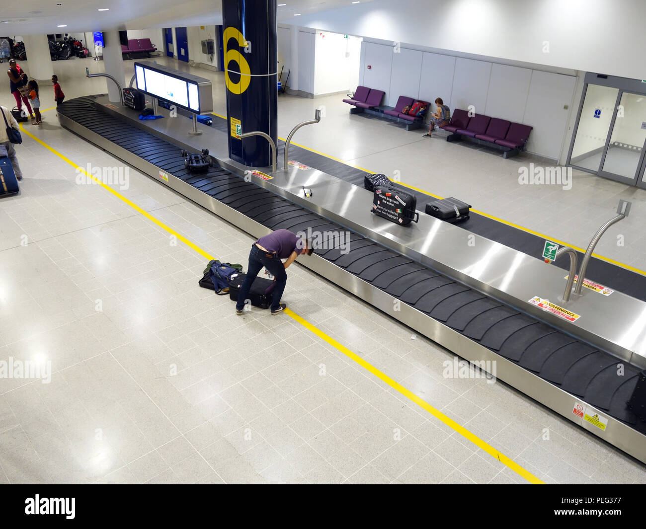 Male traveler waiting at collection conveyor belt number 6 in Terminal three at Manchester International Airport Arrivals Hall Stock Photo