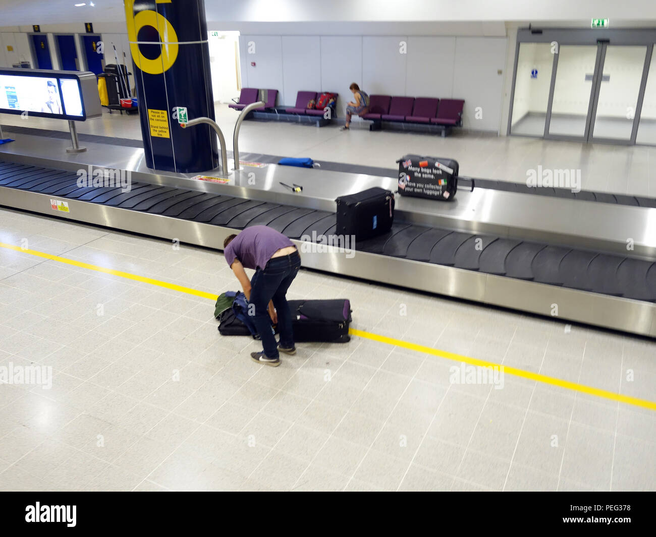 Male traveler waiting at collection conveyor belt number 6 in Terminal three at Manchester International Airport Arrivals Hall Stock Photo