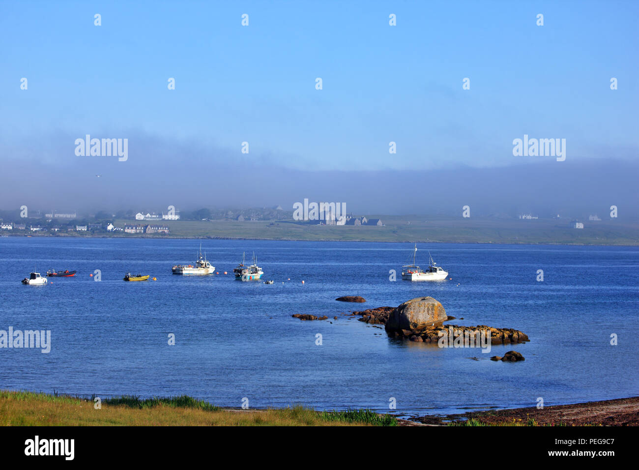 Sea mist coming in from the Atlantic Ocean over the Isle of Iona with boats, in the foreground, moored off Fionnphort on the Isle of Mull Stock Photo