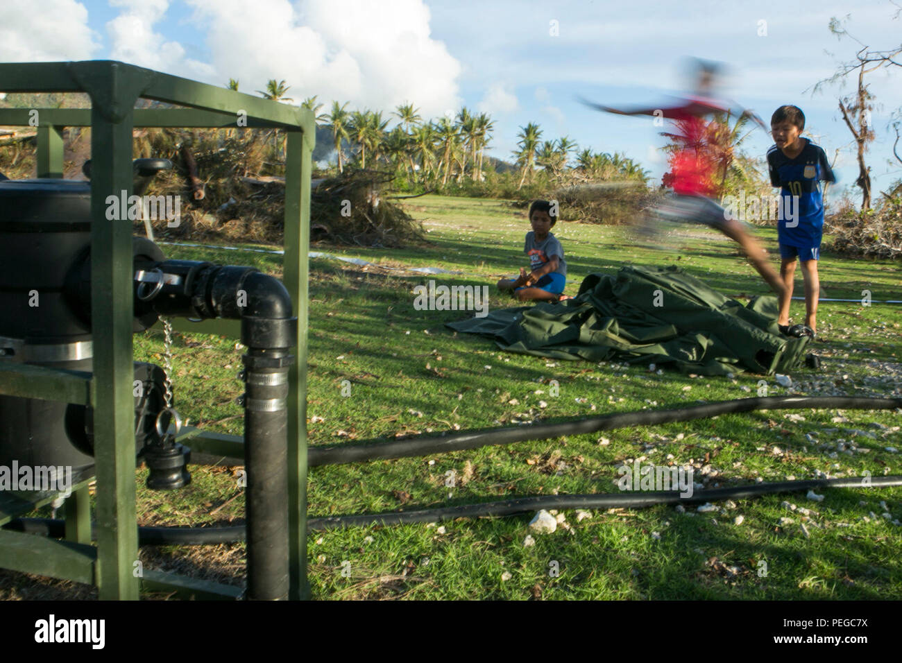Local children jump over a storage bag from a Light Weight Purification System belonging to Combat Logistics Battalion, 31st Marine Expeditonary Unit, at a water purification site in Saipan, Aug. 10, 2015. The LWPS will be used to turn seawater into potable water for the people of Saipan. The 31st MEU and the ships of the Bonhomme Richard Amphibious Ready Group are assisting federal and local agencies with distributing emergency relief supplies to Saipan after it was struck by Typhoon Soudelor, Aug. 2-3. (U.S. Marine Corps photo by Lance Cpl. Brian Bekkala/Released) Stock Photo