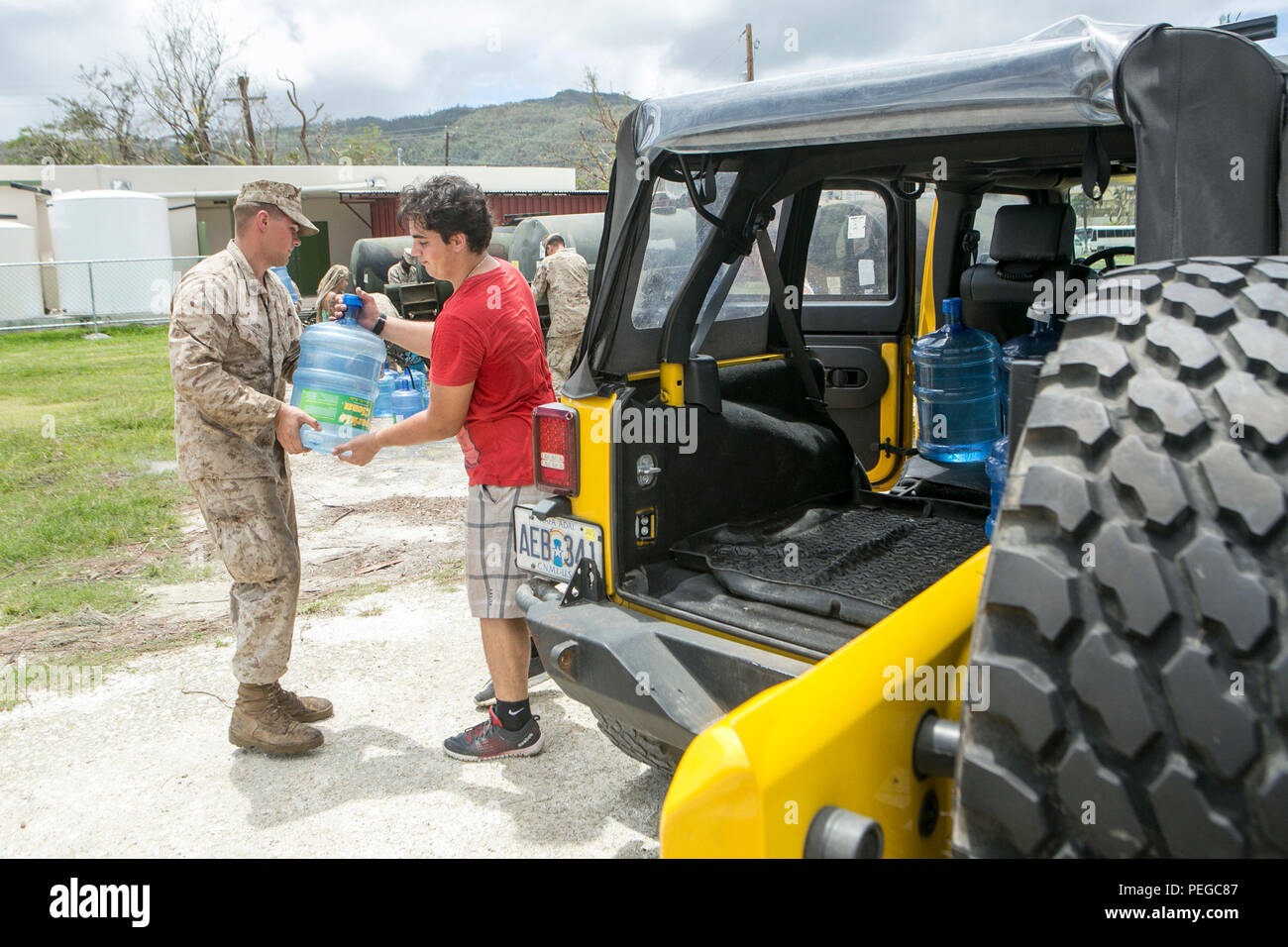 U.S. Marine Cpl. Harley Santic, with Combat Logistics Battalion 31, 31st Marine Expeditionary Unit, helps a civilian carry water to his vehicle as part of typhoon relief efforts in Saipan, Aug. 11, 2015. The 31st MEU and the ships of the Bonhomme Richard Amphibious Ready Group are assisting the Federal Emergency Management Agency with distributing emergency relief supplies to Saipan after the island was struck by Typhoon Soudelor, Aug. 2-3. (U.S. Marine Corps photo by Lance Cpl. Brian Bekkala/Released.) Stock Photo