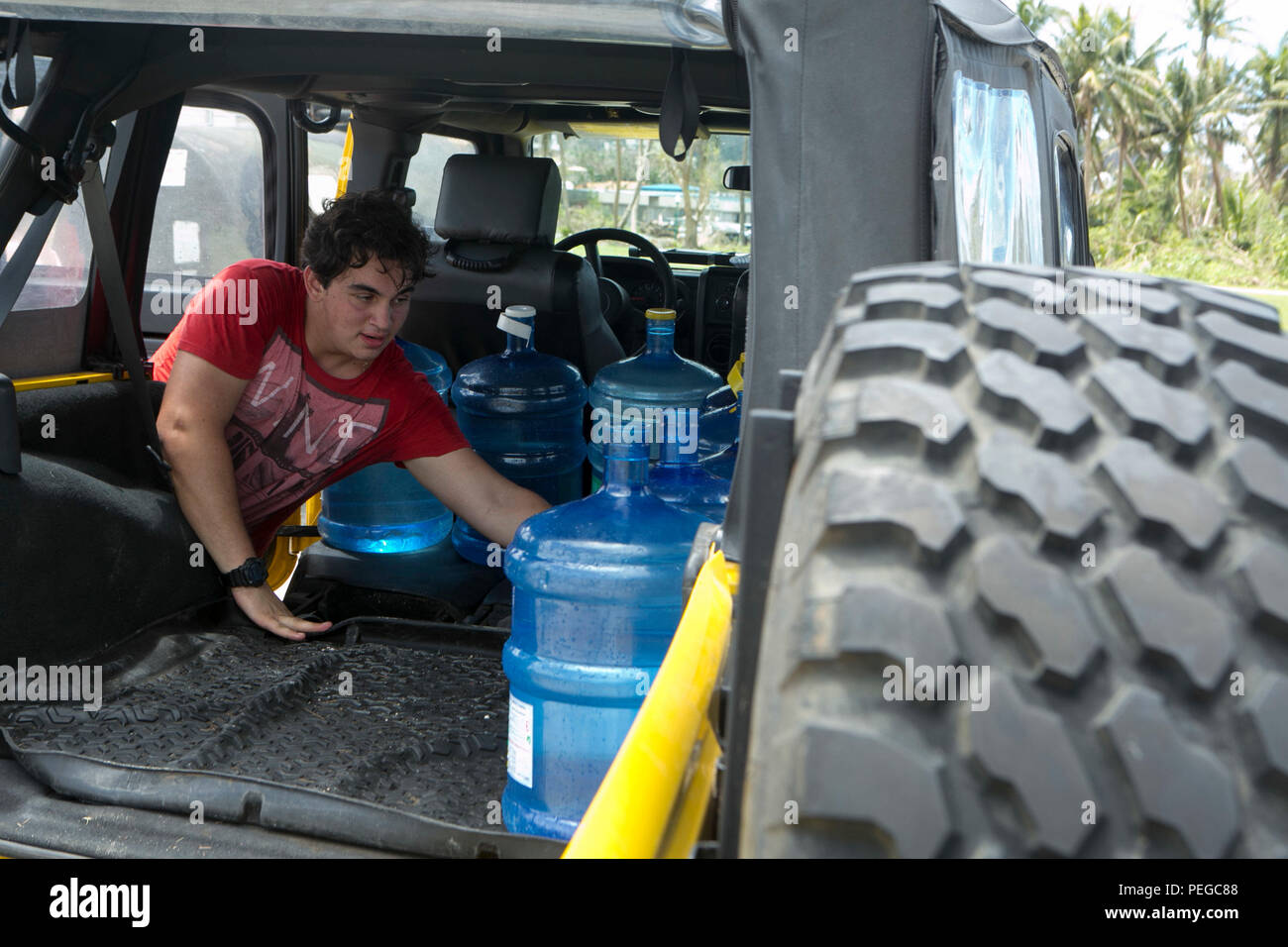 A local man places a water jug in his Jeep at a water distribution site set up by Marines with Combat Logistics Battalion 31, 31st Marine Expeditionary Unit, as part of typhoon relief efforts in Saipan, Aug. 11, 2015. The 31st MEU and the ships of the Bonhomme Richard Amphibious Ready Group are assisting the Federal Emergency Management Agency with distributing emergency relief supplies to Saipan after the island was struck by Typhoon Soudelor, Aug. 2-3. (U.S. Marine Corps photo by Lance Cpl. Brian Bekkala/Released.) Stock Photo