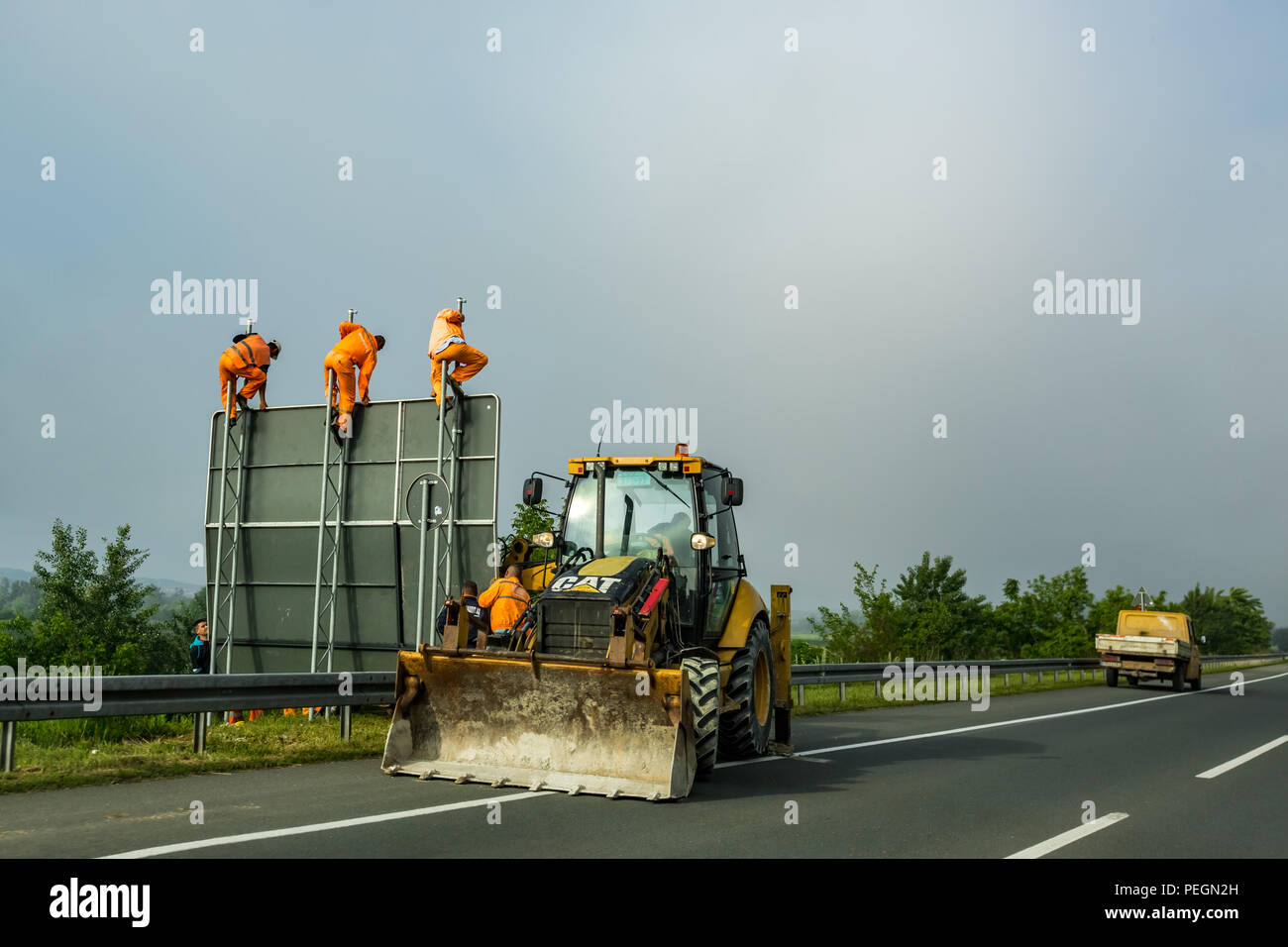 BELGRADE, SERBIA - MAY 15, 2017: Three men in orange work suits put up new traffic board sign on a newly reconstructed major road near Serbian capital city of Belgrade in a hazy day Stock Photo