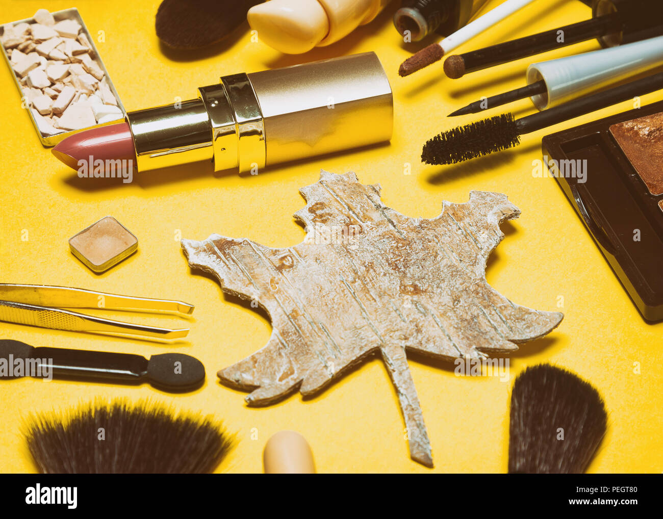 Autumn makeup in retro style. Make-up products brown and golden colors with maple leaf made of bark. Side view, selective focus Stock Photo