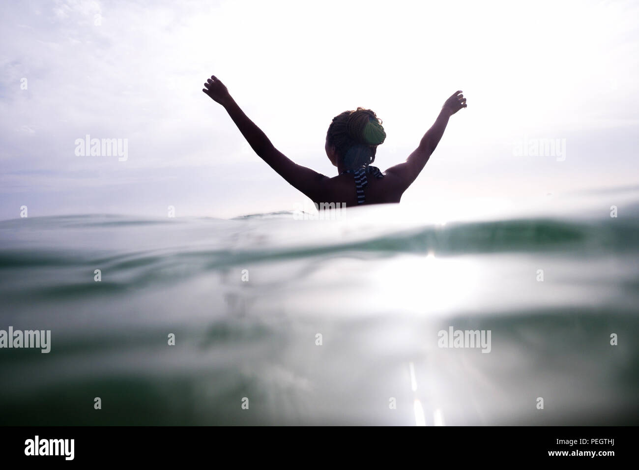 A woman standing in the sea with her back to the camera her arms are up ...