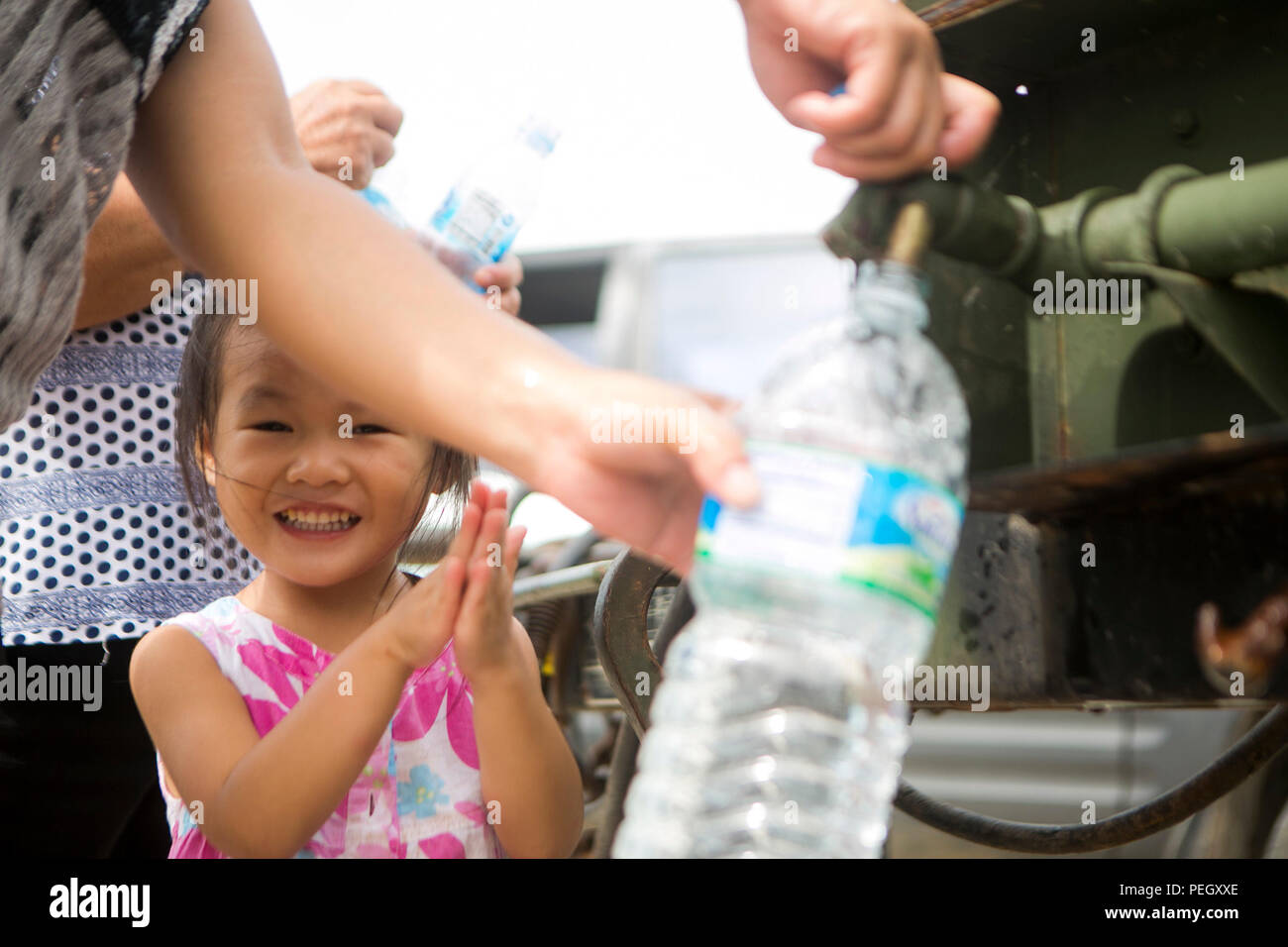 A young girl watches her parents fill water bottles while U.S. Marines with Combat Logistics Battalion 31, 31st Marine Expeditionary Unit, distribute water to local civilians during typhoon relief efforts in Saipan, Aug. 13, 2015. The Marines and sailors of the 31st MEU assisted the people of Saipan by producing and distributing potable water. The MEU was conducting training near the Mariana Islands when it was redirected to Saipan after the island was struck by Typhoon Soudelor Aug. 2-3. (U.S. Marine Corps photo by Lance Cpl. Brian Bekkala/Released) Stock Photo