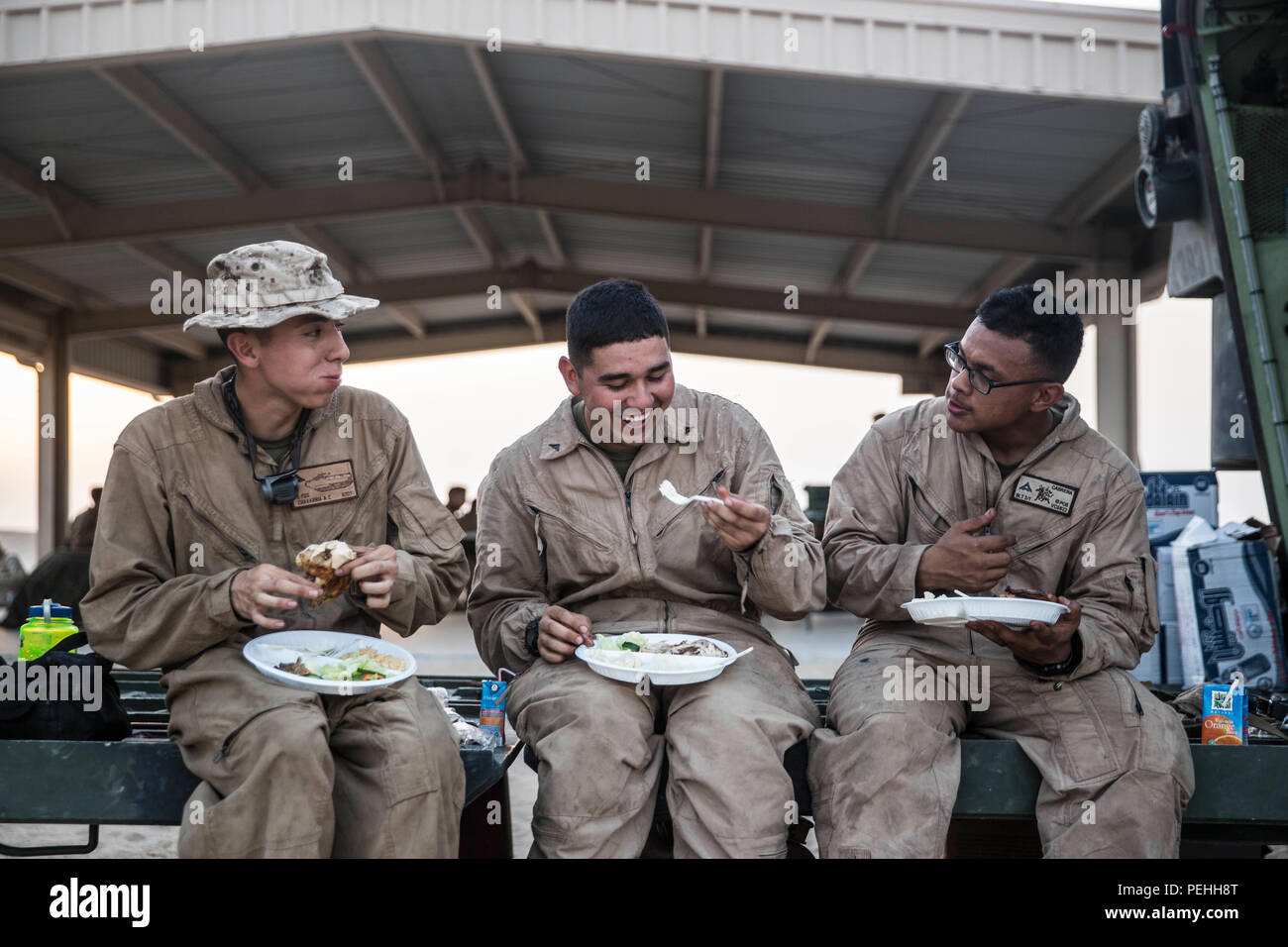 KUWAIT (Aug. 18, 2015) U.S. Marine Lance Cpl. Alejandro Chavarria (left), Lance Cpl. David Medina and Lance Cpl. Anthony Cabrera enjoy a hot meal in the field after a live-fire and maneuver exercise. Chavarria, Medina, and Cabrera are all crewmen with Kilo Company, Battalion Landing Team 3rd Battalion, 1st Marine Regiment, 15th Marine Expeditionary Unit (MEU). During the training, Marines with Combat Logistics Battalion 15, 15th MEU, delivered hot meals to the Marines in the training areas. Elements of the 15th MEU are ashore in Kuwait for sustainment training to maintain and enhance the skill Stock Photo
