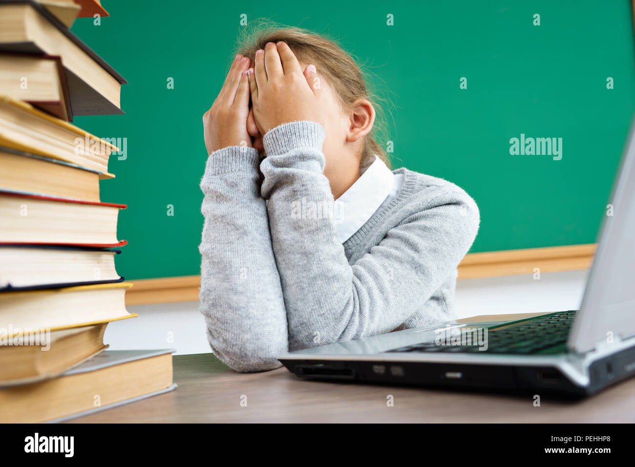 Schoolgirl closed her eyes and crying. Photo of little girl in classroom around books. Education concept Stock Photo
