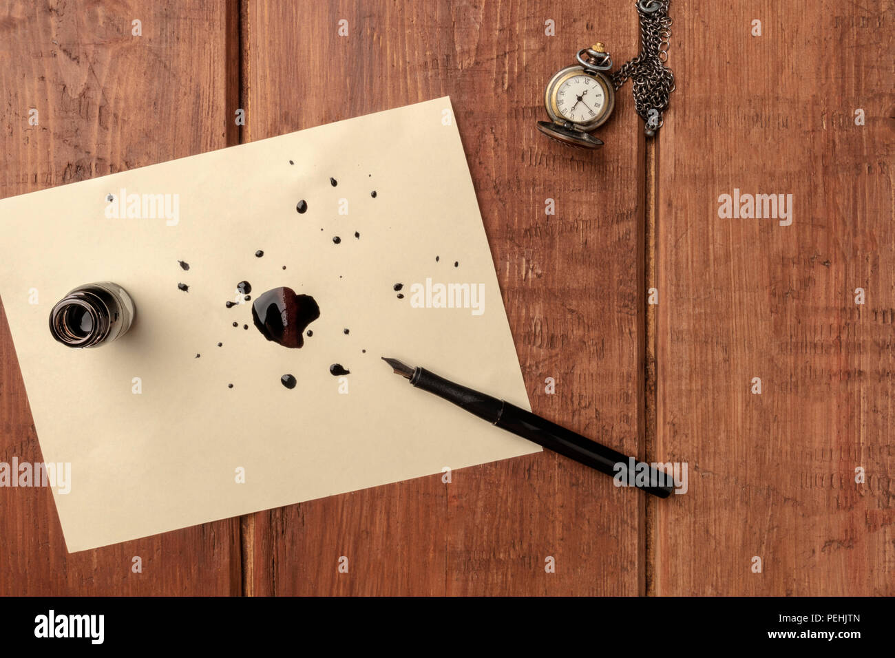 An overhead photo of an ink well with drops of ink and a nib pen, with ...