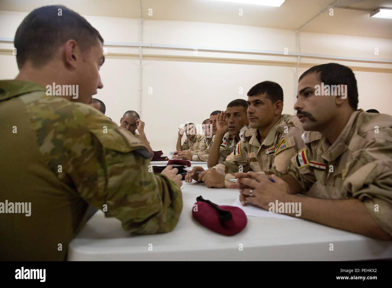 An Australian soldier assigned to Task Group Taji speaks to a group of Iraqi soldiers attending the noncommissioned officer academy at Camp Taji, Iraq, Aug. 22, 2015. Task Group Taji spearheaded the academy concept in order to teach Iraqi NCOs how to train and care for their soldiers in different situations. Through professional development with the Iraqi NCOs, Combined Joint Task Force – Operation Inherent Resolve is empowering the Iraqi security forces in the fight against the Islamic State of Iraq and the Levant. (U.S. Army photo by Spc. Paris Maxey/Released) Stock Photo