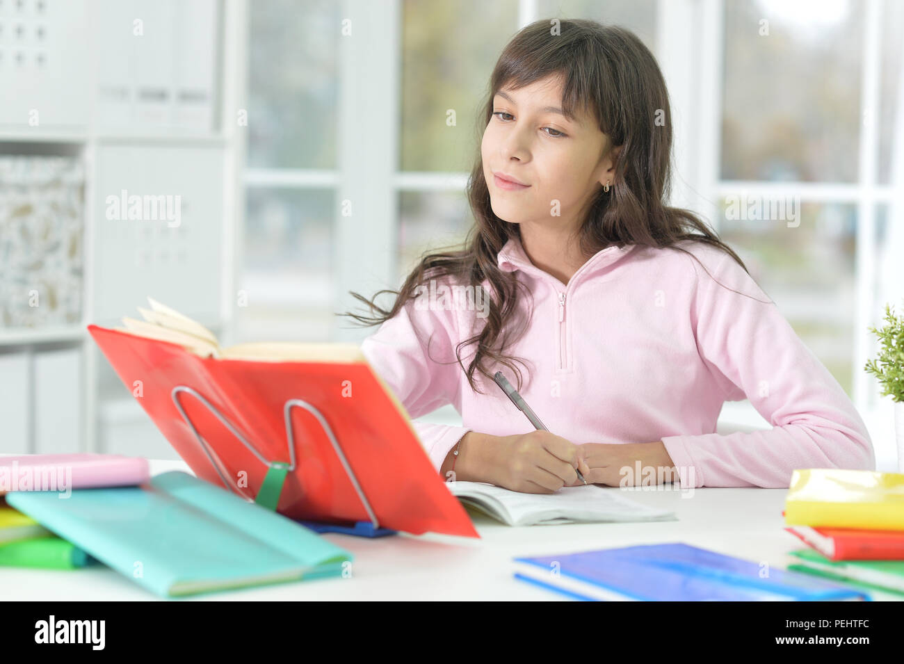 Happy schoolgirl sitting at desk and studying Stock Photo - Alamy