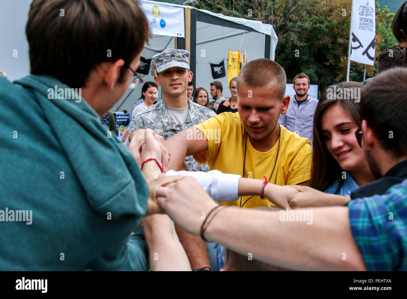 Sgt. Mark Leffew, a U.S. Army Reserve Soldier deployed to Kosovo with the 345th Combat Support Hospital, watches as a group of festival-goers try to untangle themselves while playing a 'human knot' game Aug. 22, 2015, in the main square of Peja, Kosovo, during the sixth annual Anibar International Animation Festival. Leffew volunteered his time to support the Pristina Rotary Club’s Violence-Free Future project, which aims to promote pro-social behaviors among Kosovo’s youth. Leffew and the 345th CSH serve as Multinational Battle Group-East’s Task Force Medical, serving on the 20th iteration of Stock Photo