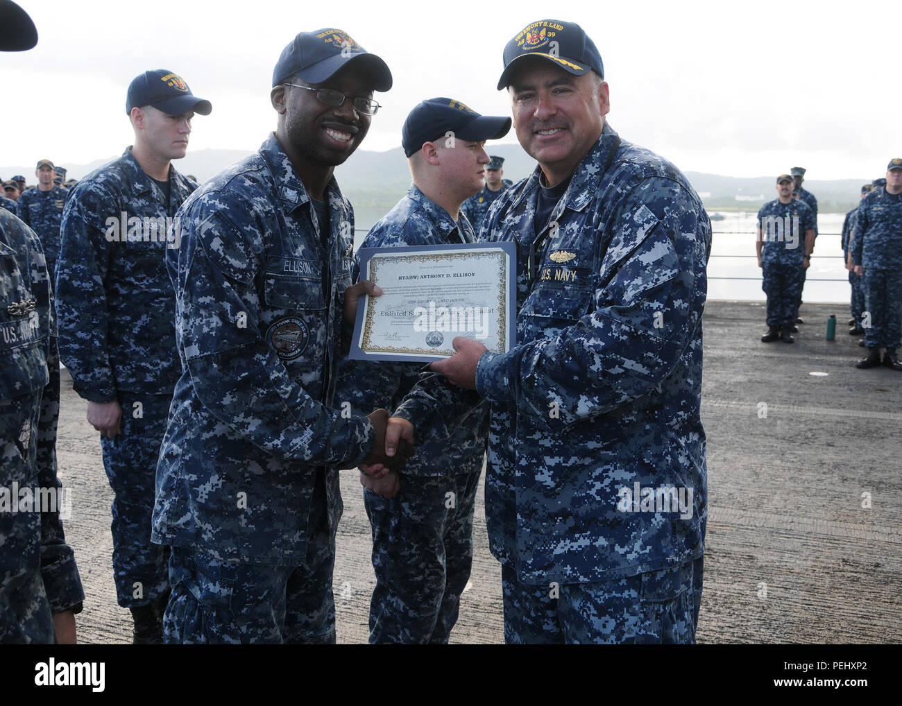 150828-N-VH871-002 U.S. NAVAL BASE GUAM (Aug. 28, 2015) – Capt. Mark A. Prokopius, commanding officer of submarine tender USS Emory S. Land (AS 39) presents Hull Technician 3rd Class Anthony Ellison with a certificate for completing his Enlisted Surface Warfare Specialist (ESWS) qualification. Sailors spend significant time working and studying to complete ESWS and upon completion have an extensive level of knowledge about shipboard departments, capabilities, damage control, force protection, supply, U.S. Navy heritage, and engineering.  Emory S. Land is a forward deployed expeditionary submar Stock Photo