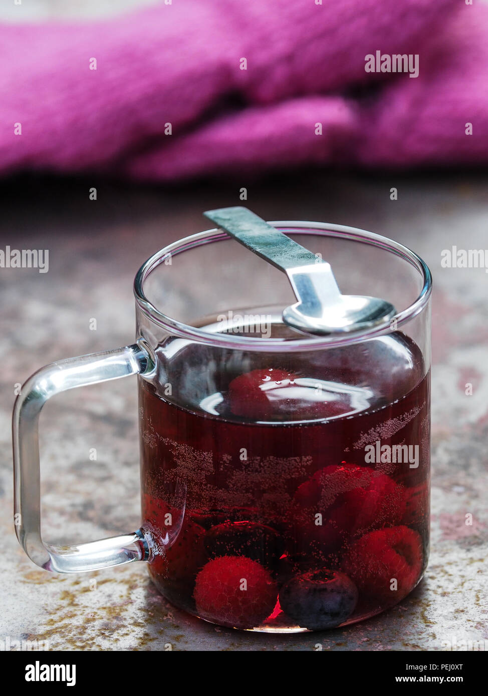 Mulled wine with berry fruits on an old red lacquered metal table with gloves in the background. Stock Photo