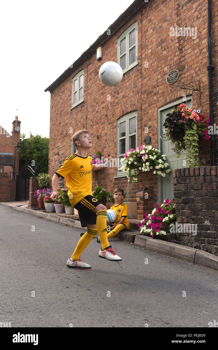 Boys in Wolverhampton Wanderers FC replica kits playing football outside the birthplace of Wolves and England footballing legend Billy Wright in Ironb Stock Photo