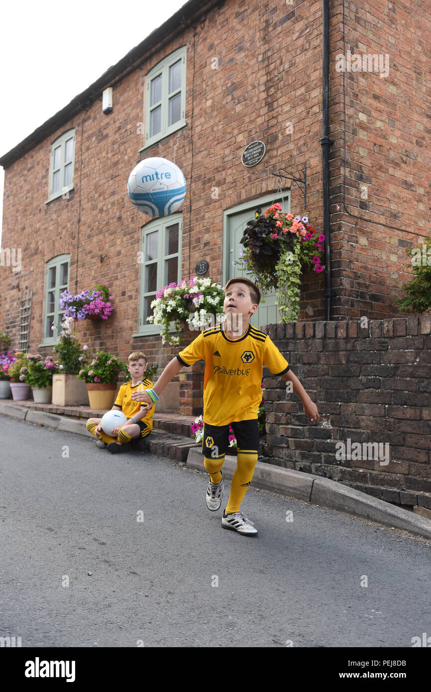 Boys in Wolverhampton Wanderers FC replica kits playing football outside the birthplace of Wolves and England footballing legend Billy Wright in Ironb Stock Photo
