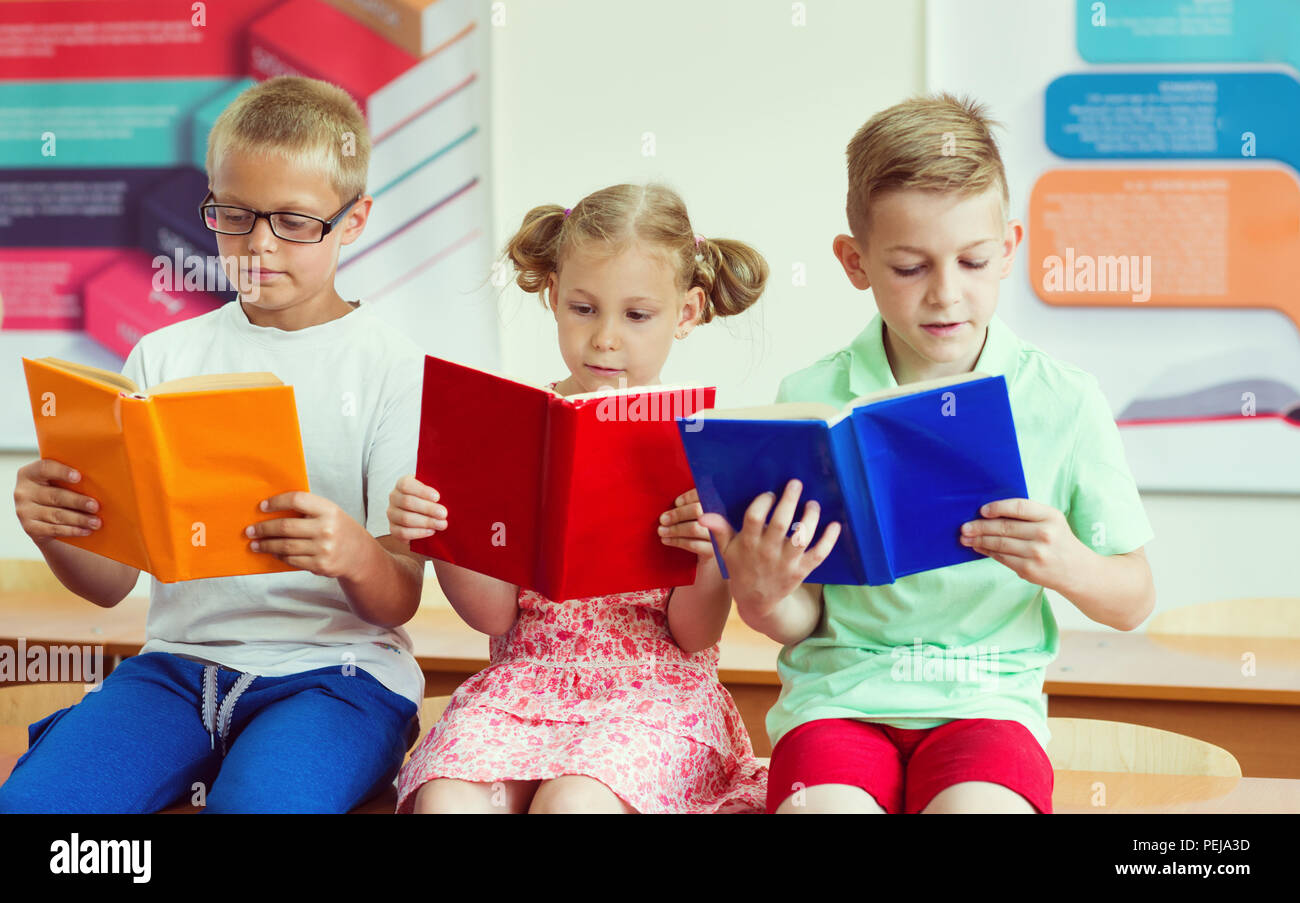 Three schoolchildren reading books in classroom at school Stock Photo ...